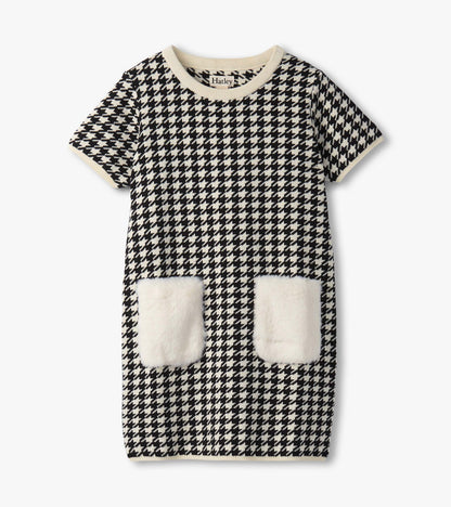 Black and white houndstooth sweater dress featuring faux fur pockets and a ribbed neckline. Short sleeves, knee-length desig…