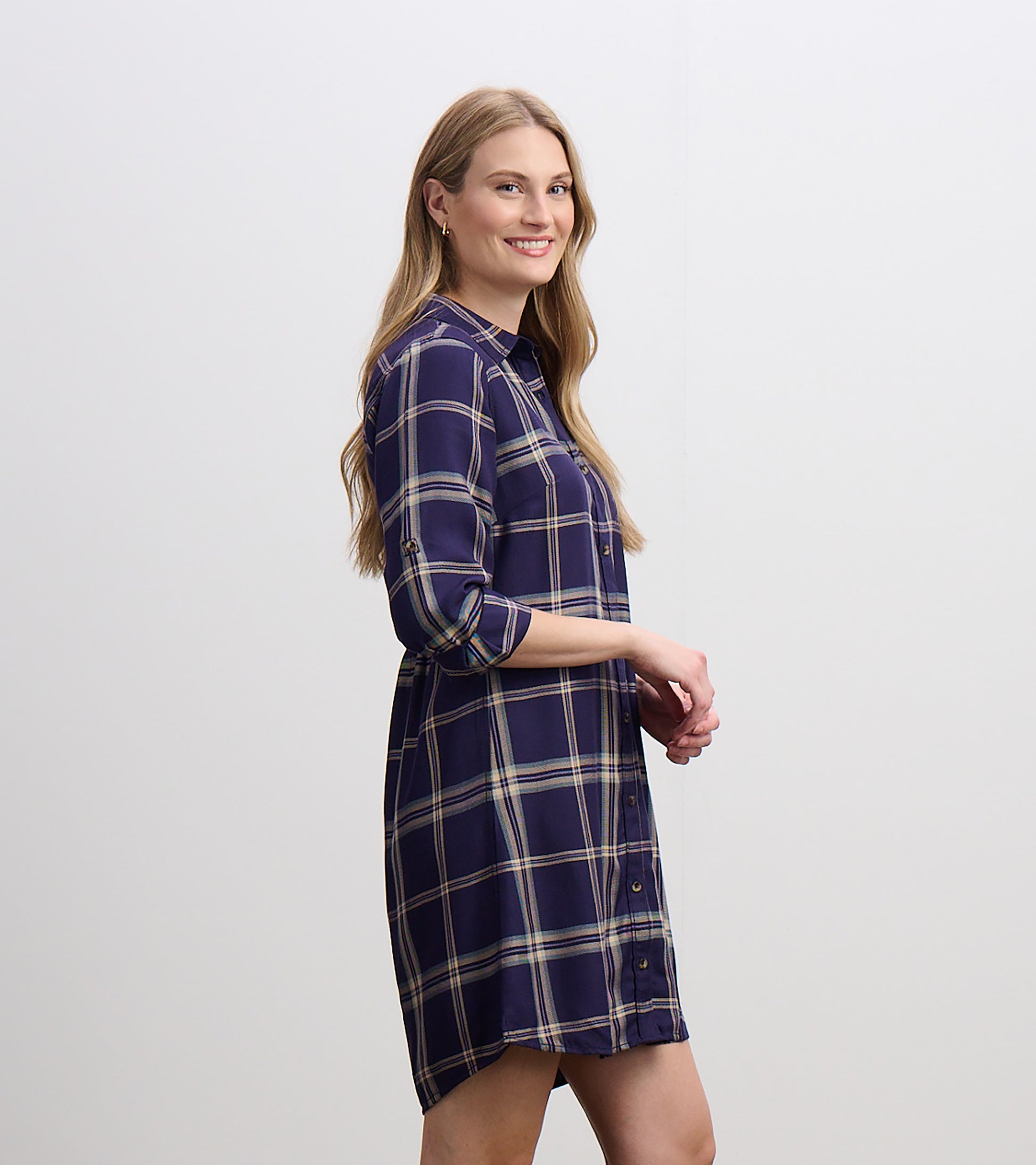 Side view of navy plaid shirt dress with collar, button front, rolled sleeves, and curved hem