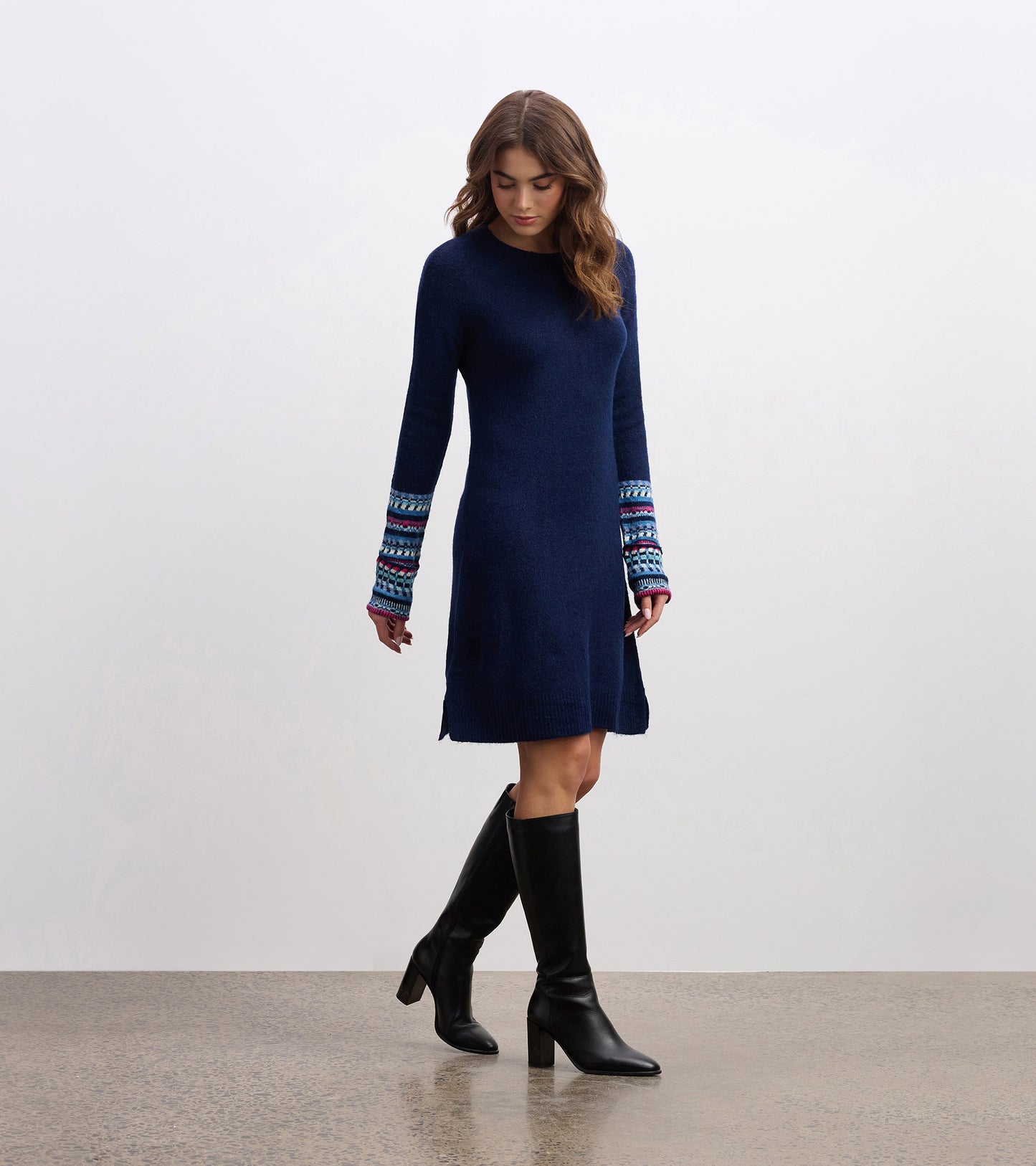 Navy sweater dress with long sleeves featuring colorful patterned cuffs, styled with knee-high black boots.