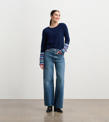 Navy sweater with patterned cuffs, paired with high-waisted jeans, worn by a model standing and smiling.