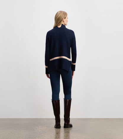 Navy mock neck sweater with a contrasting stripe at the hem, styled with fitted jeans and tall boots.