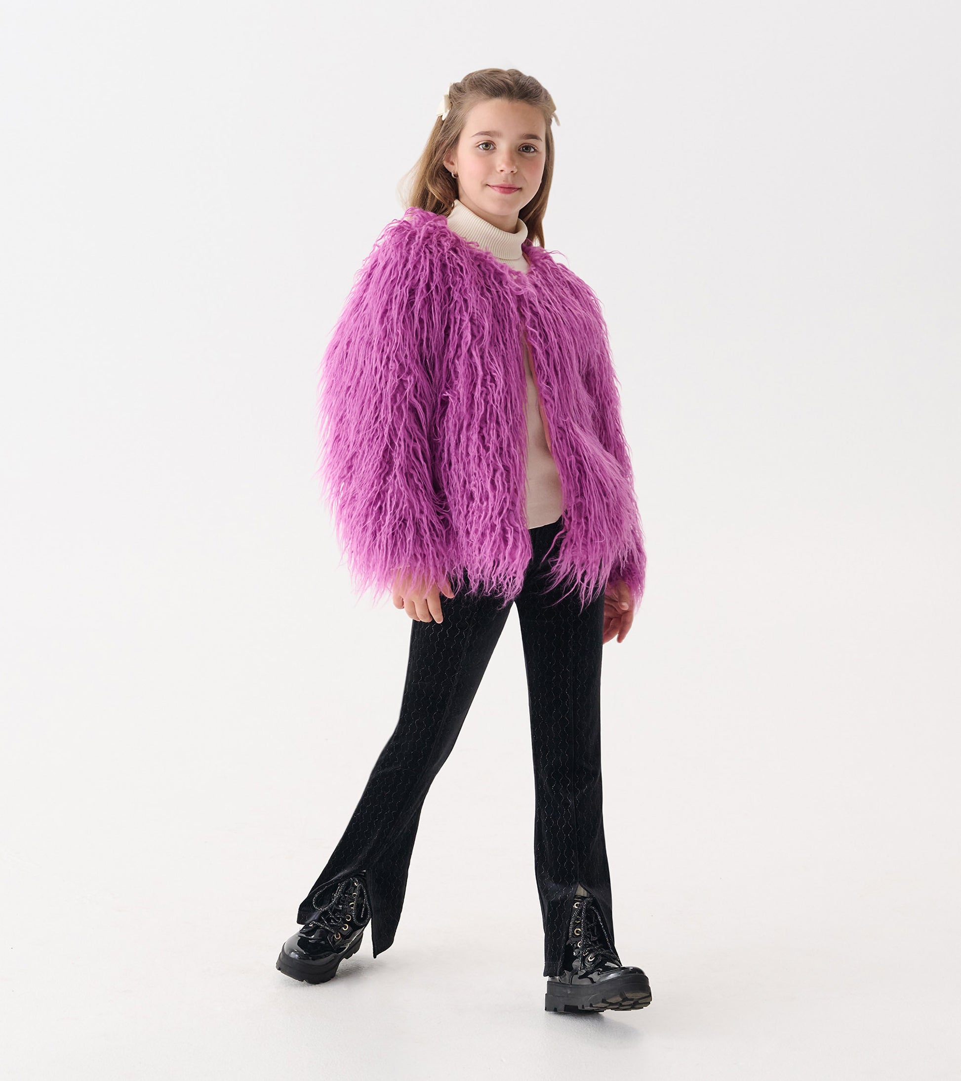 Radiant orchid faux fur topper with long sleeves, worn over a light sweater and paired with black pants and boots.