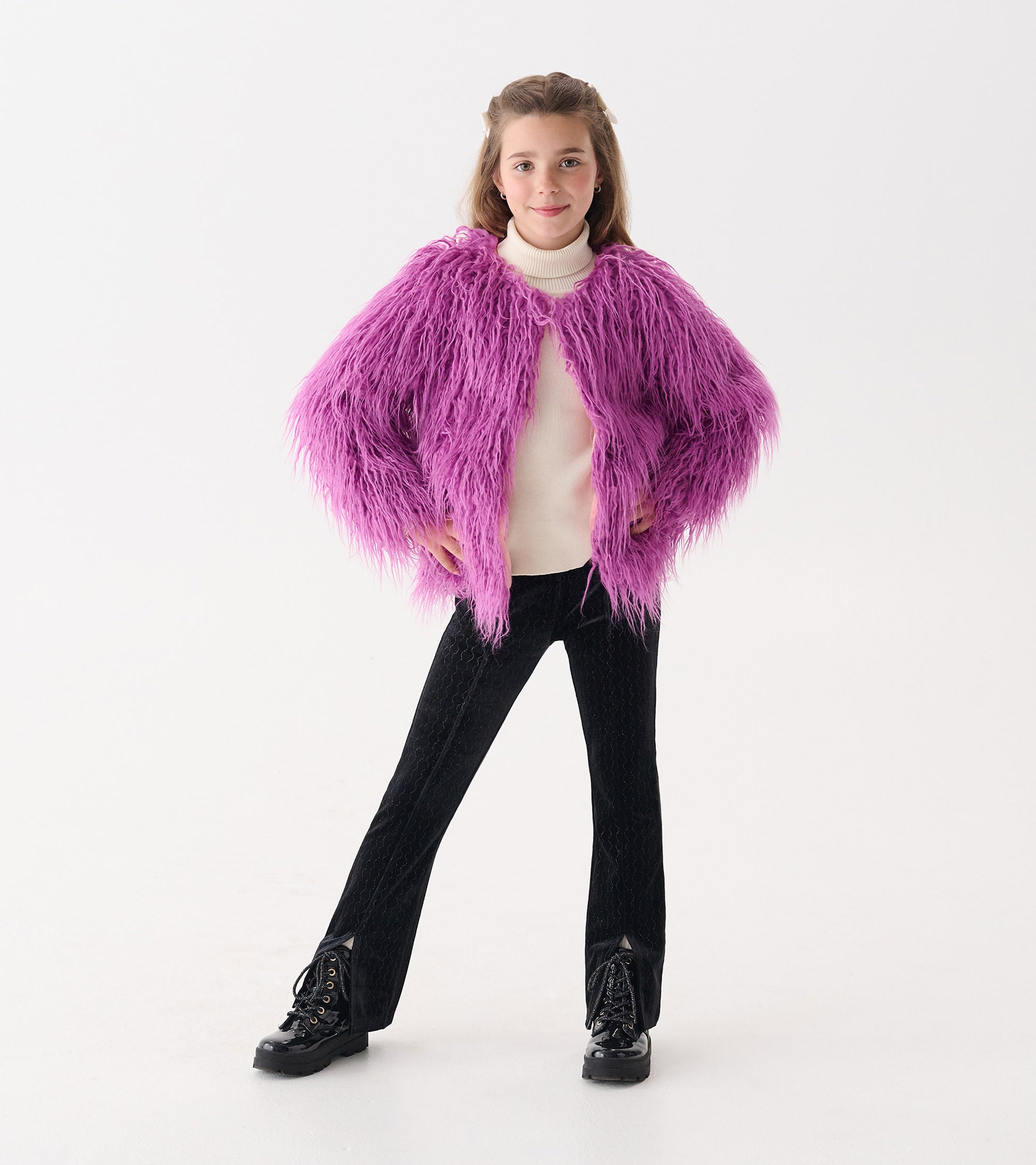 Radiant orchid faux fur topper with long sleeves, worn over a white turtleneck and paired with black pants and boots.