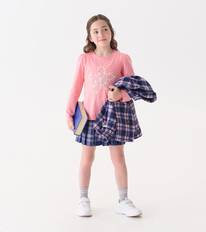 Pink puff sleeve tee with embroidered flower design, paired with a plaid skirt and holding a book and jacket.
