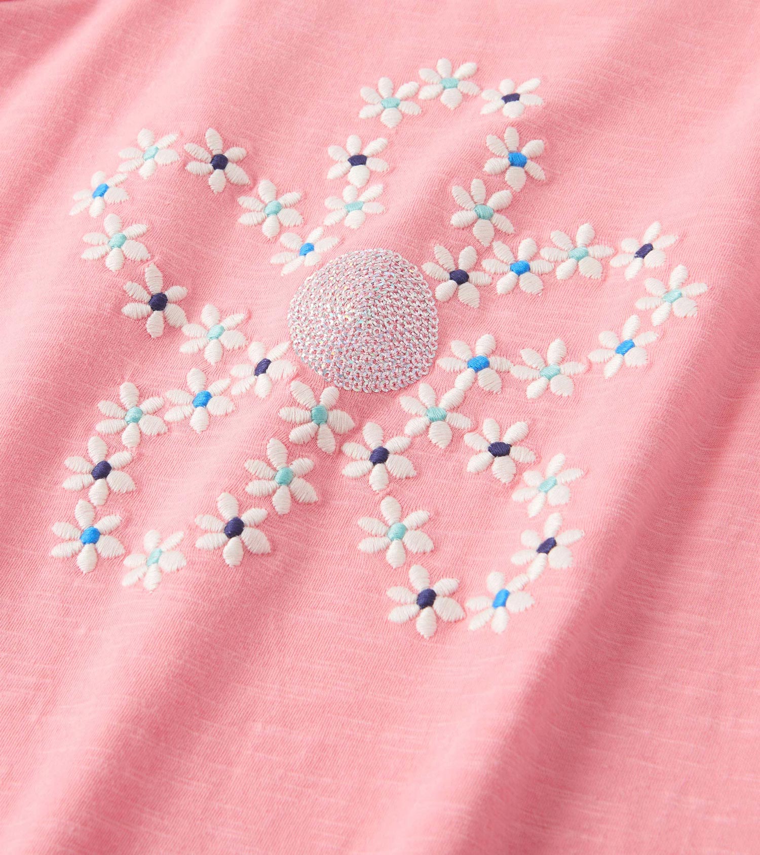 Pink graphic tee featuring embroidered flowers in white, blue, and navy, with a textured center detail.