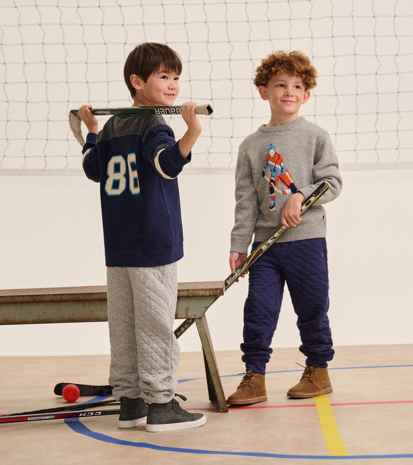 Boy in a heather gray hockey player sweater standing with a hockey stick in an indoor gym