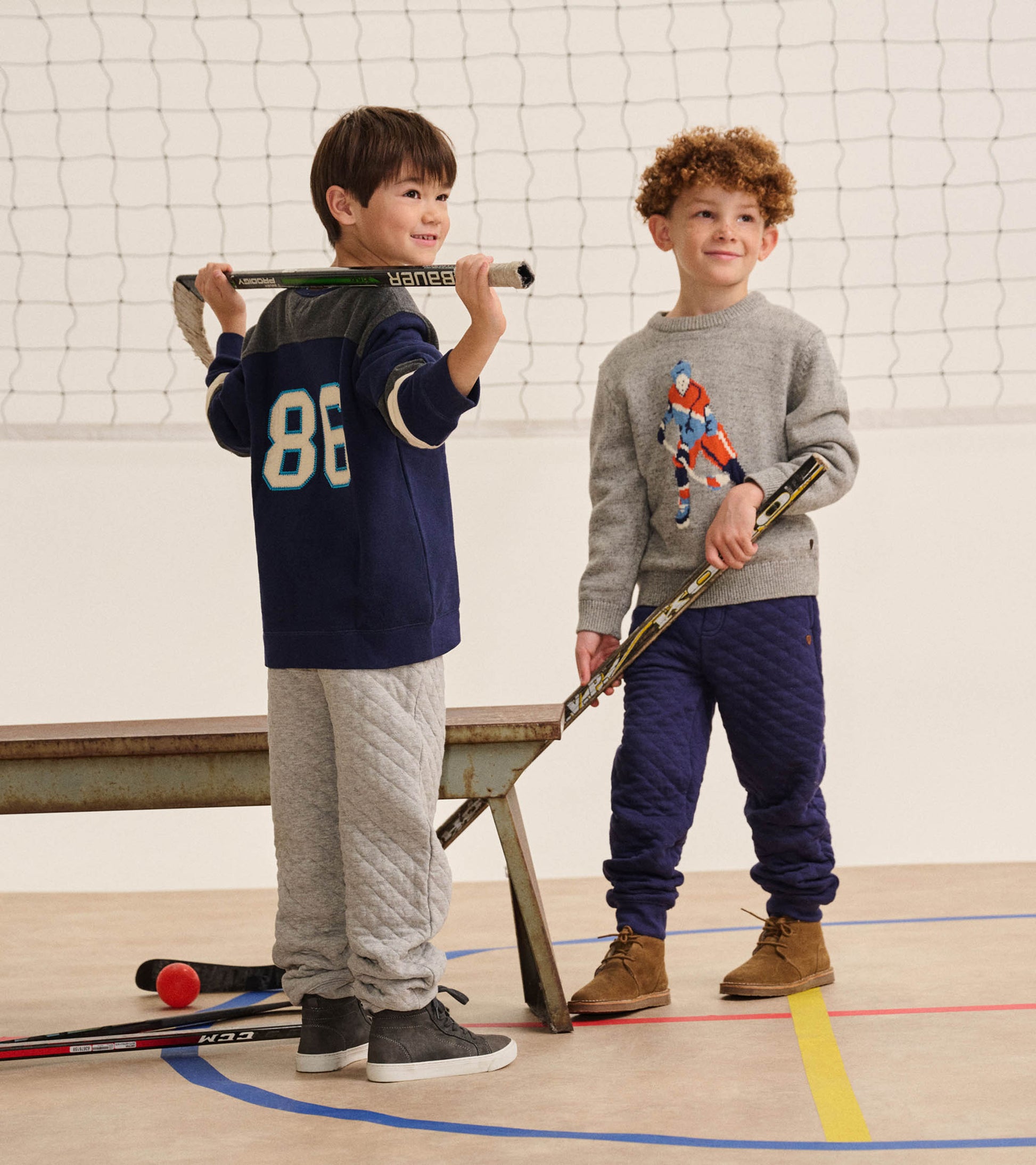 Boy in a heather gray hockey player sweater standing with a hockey stick in an indoor gym