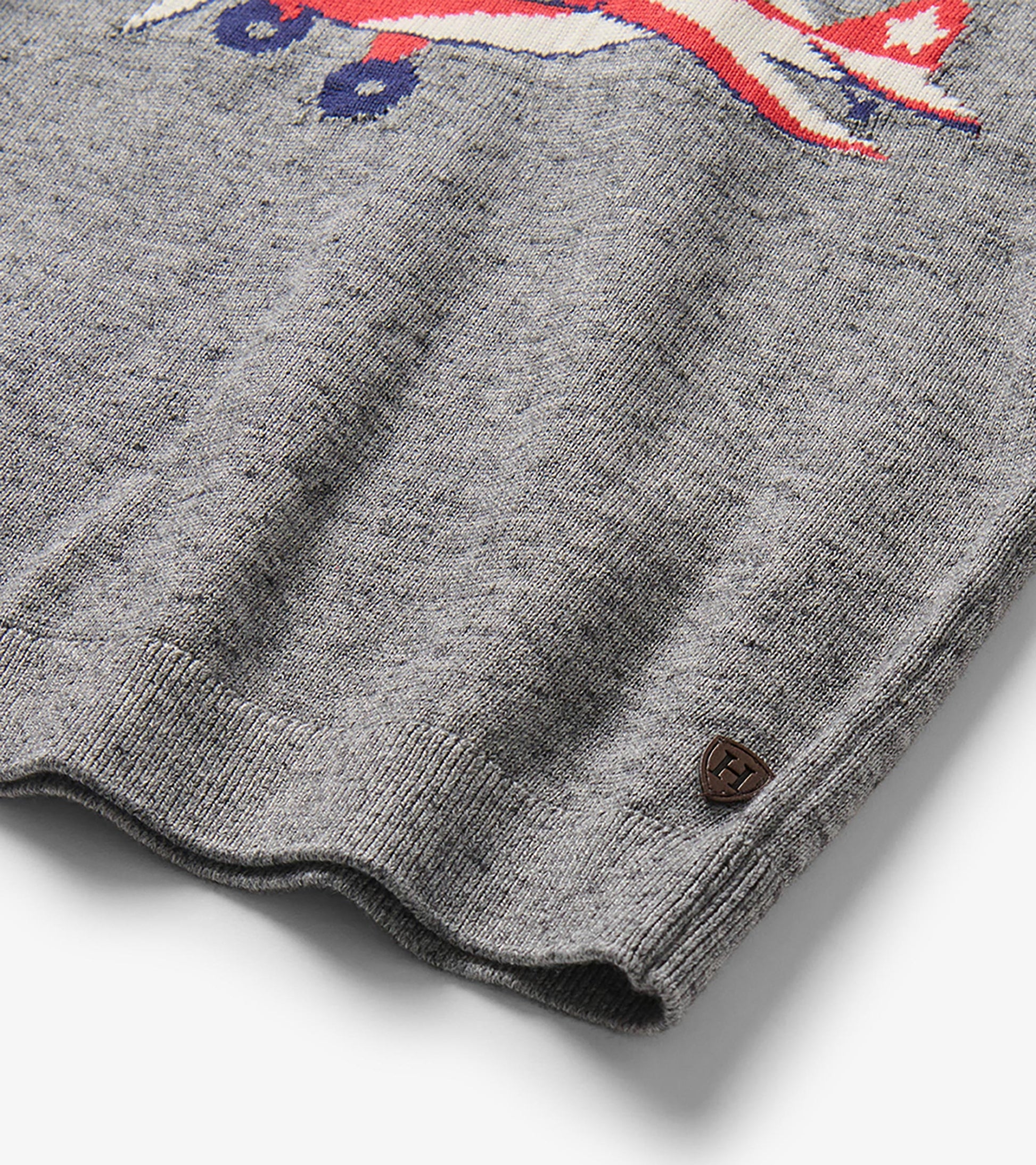 Close-up of the gray marled sweater hem with part of the plane motif and a small Hatley badge