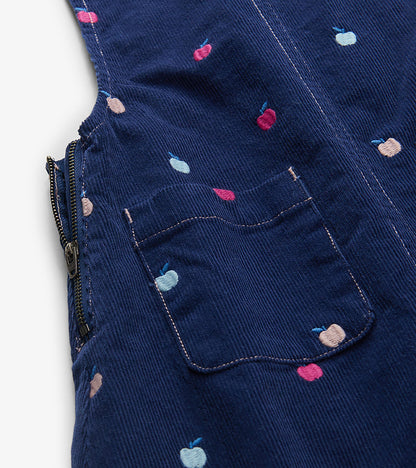 Close-up of navy pinafore dress showing embroidered apples, front pocket, and side zipper