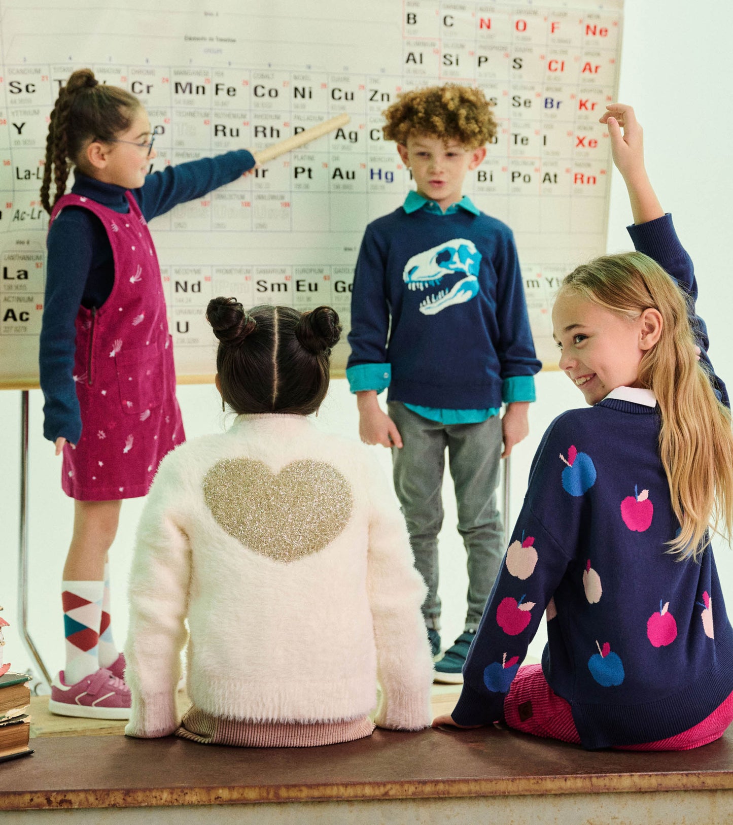 Girl wearing a navy apple-pattern sweater seated in a classroom, shown from the back and side