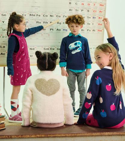 Girl wearing a navy apple-pattern sweater seated in a classroom, shown from the back and side