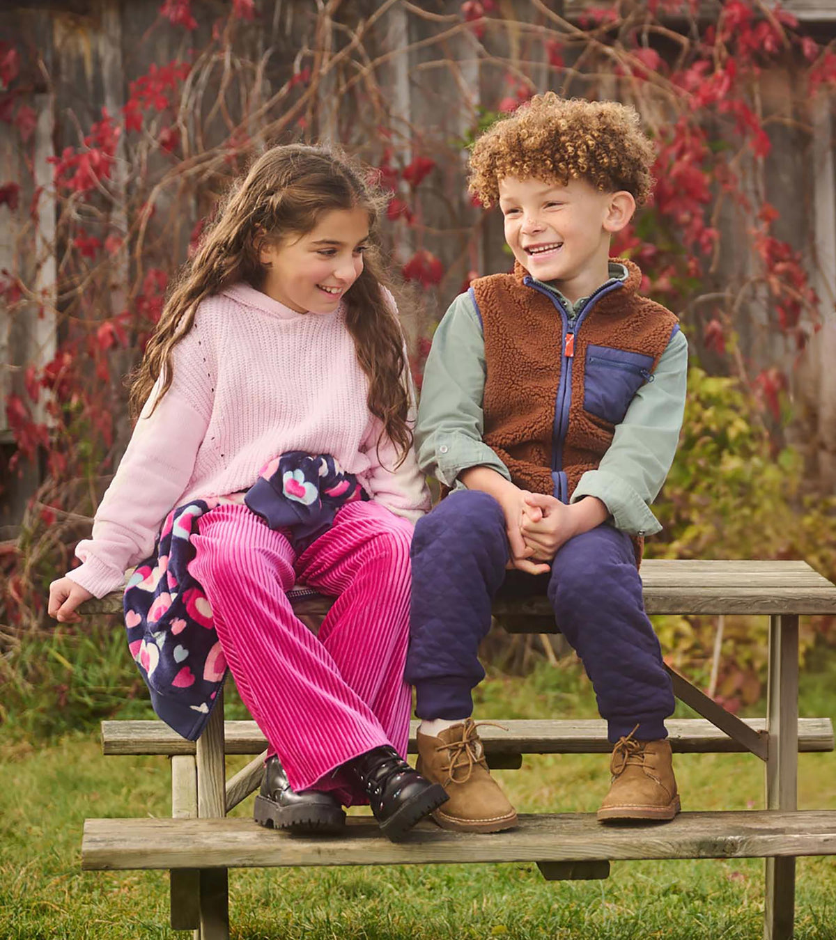 Girl wearing a light pink hooded sweater with cream heart sleeves, seated outdoors
