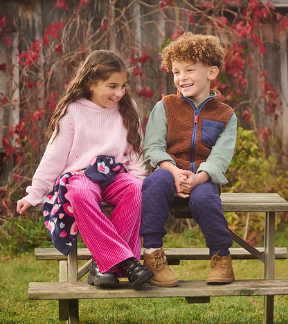 Girl wearing a light pink hooded sweater with cream heart sleeves, seated outdoors