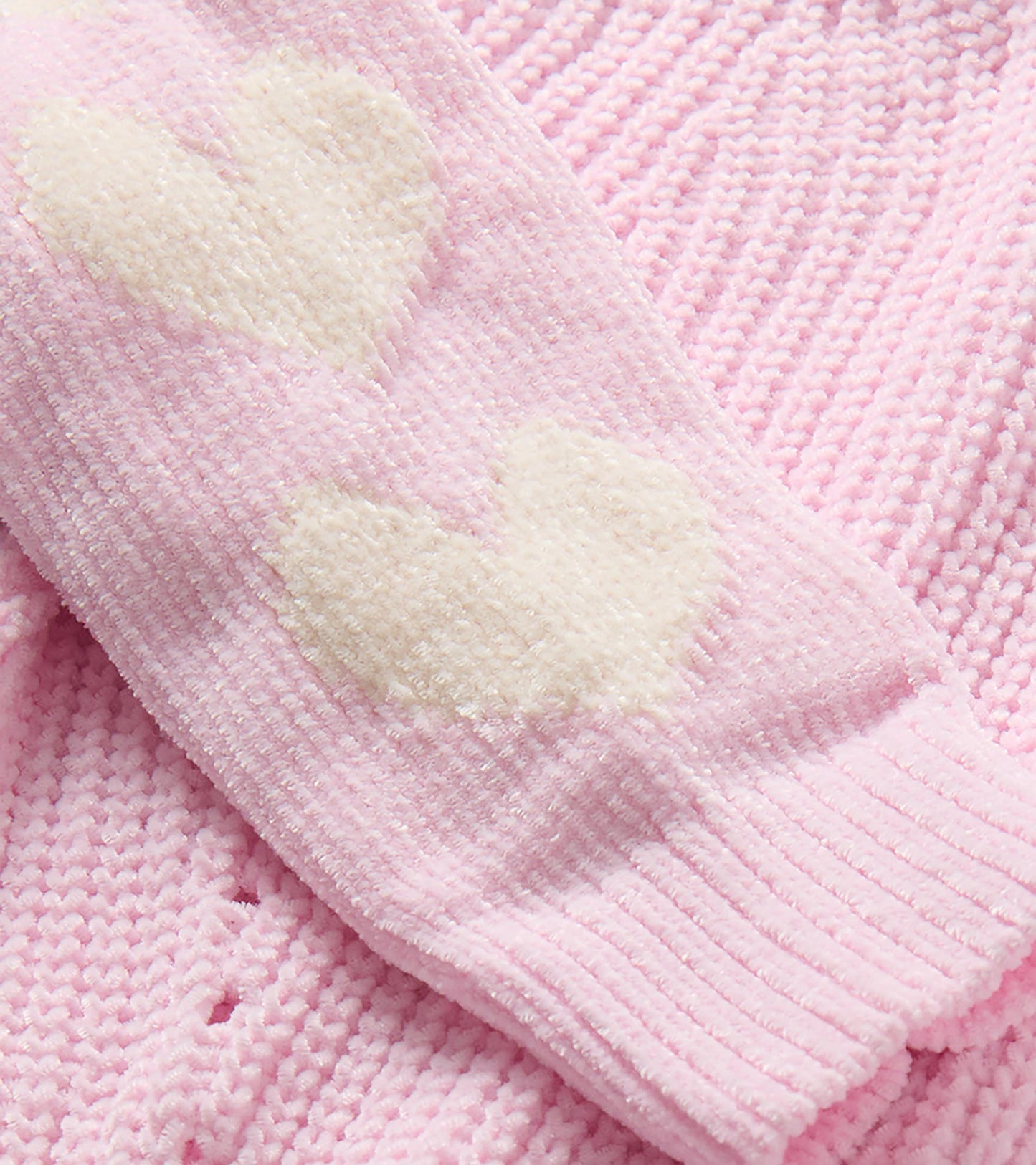 Close-up of pink knit sweater sleeve with cream heart pattern and ribbed trim