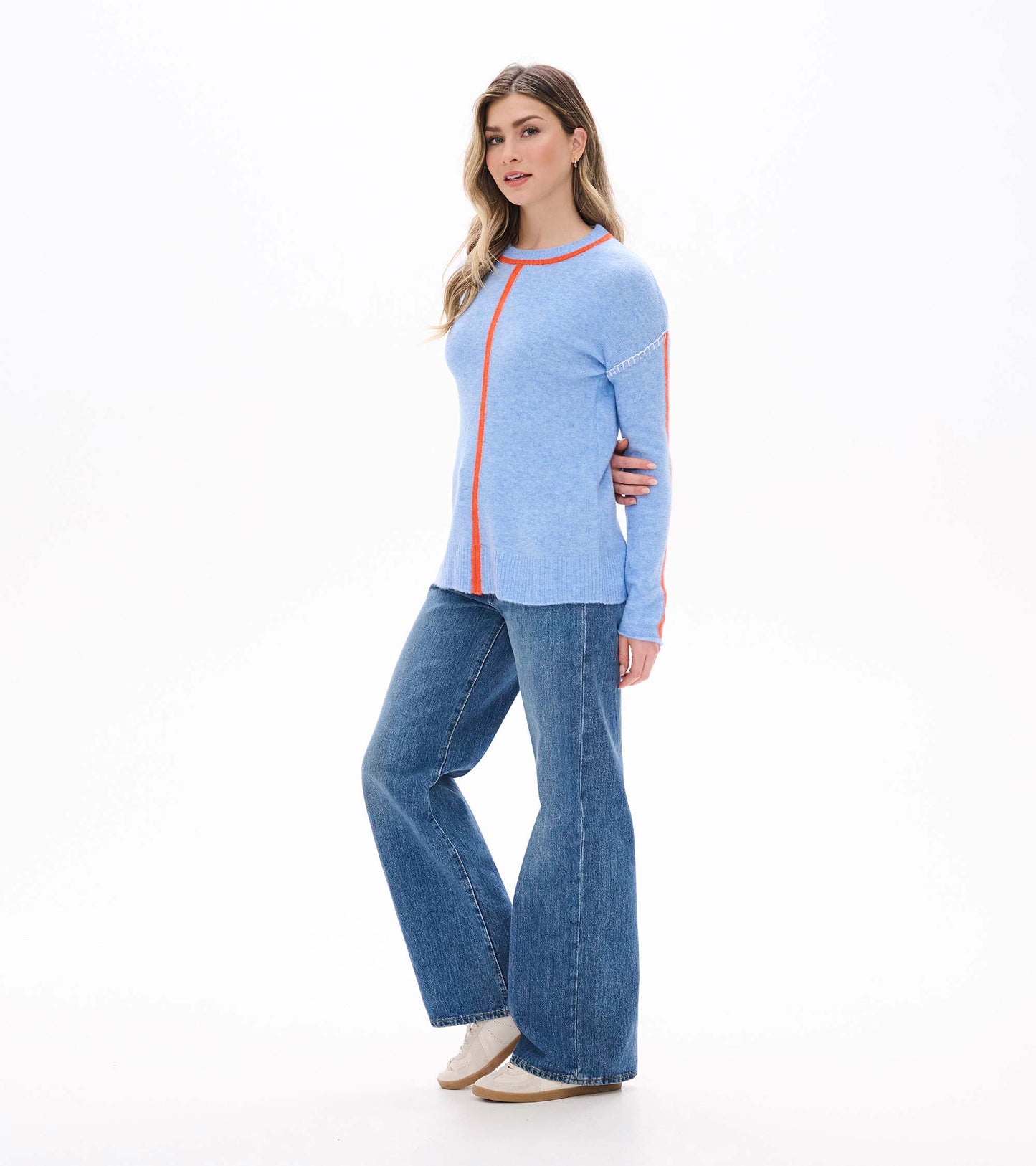 Side front view of azure blue Maeve sweater with orange stripe detail and white shoulder stitching