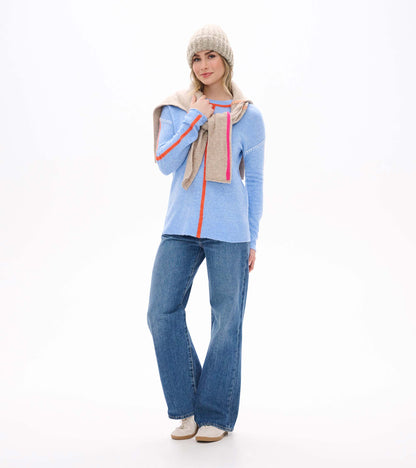 Maeve sweater in azure blue with orange trim, shown front view with jeans, scarf, and knit beanie