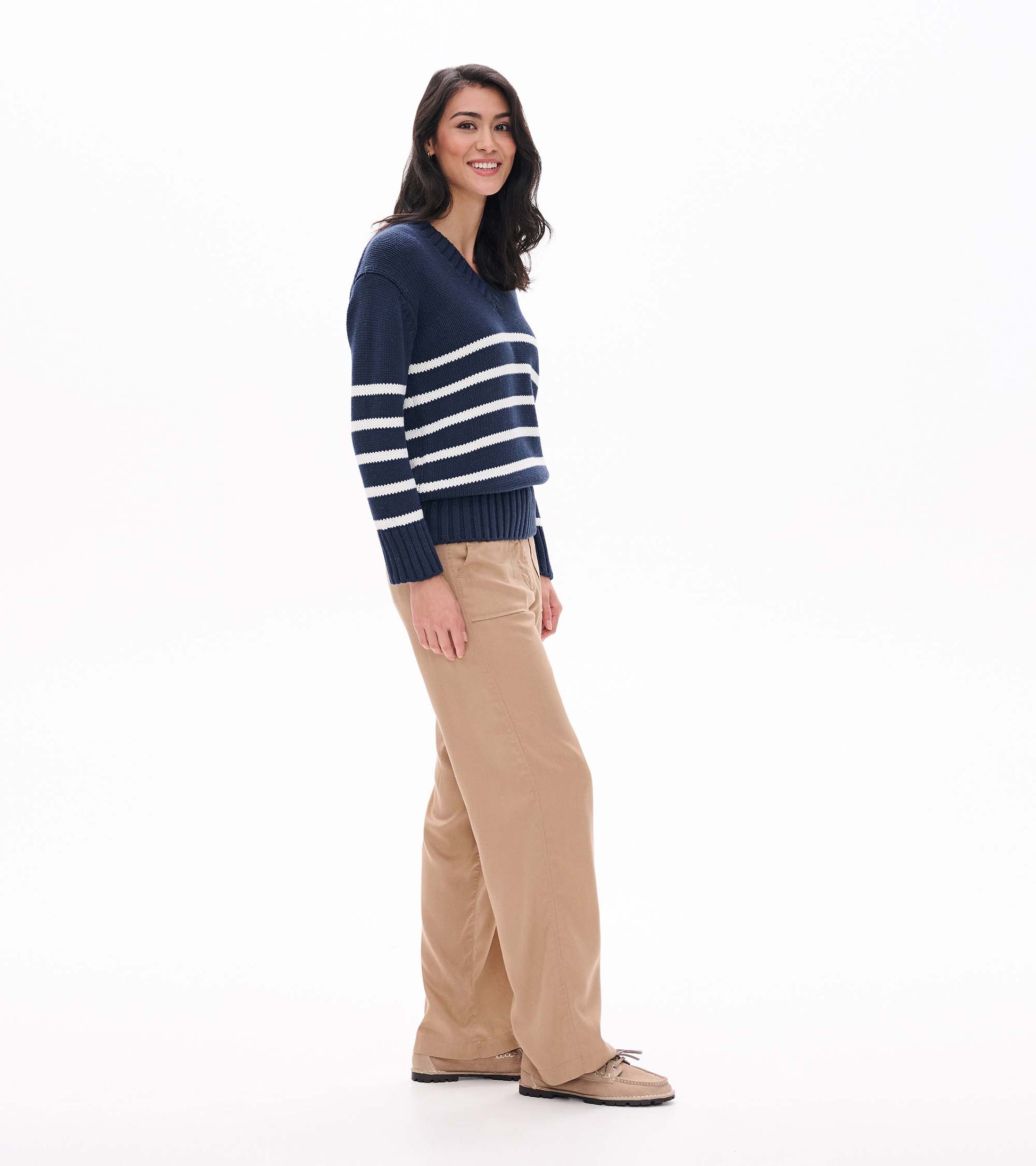 Side view of navy V-neck sweater with cream stripes and ribbed hem on model
