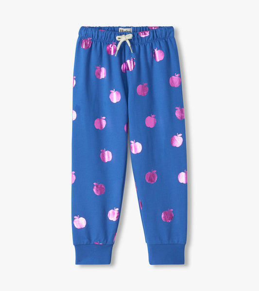 Front view of blue relaxed-fit track pants with metallic pink apple print, white drawstring, and cuffed ankles