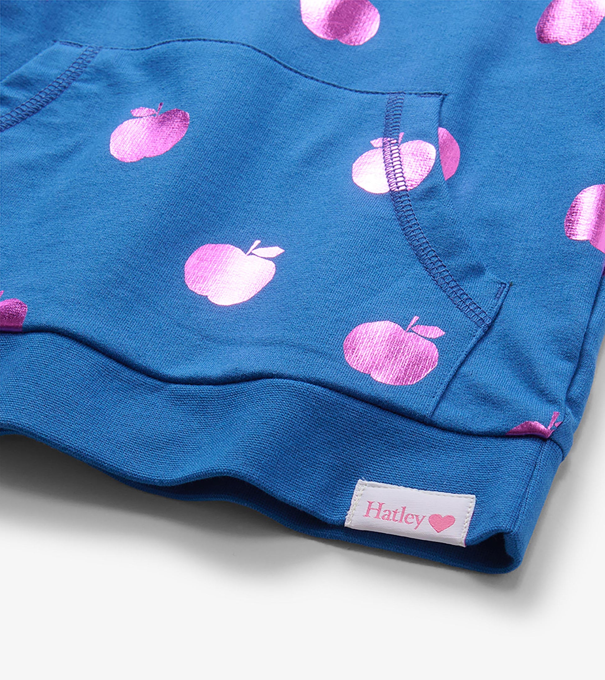 Close-up of blue pullover kangaroo pocket with pink foil apple print and visible Hatley hem label