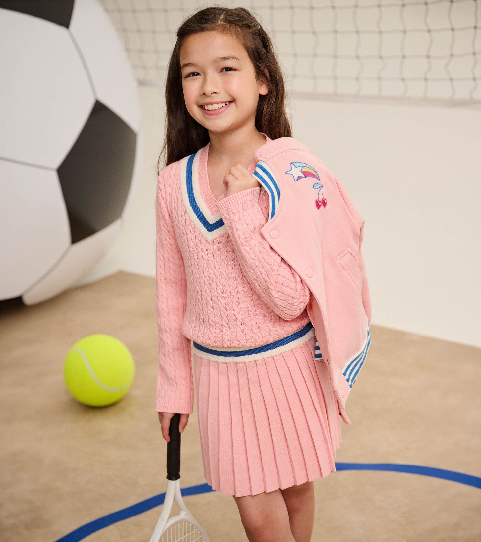 Girl holding pink varsity bomber jacket over shoulder, showing blue striped trim and embroidered shooting star and cherries