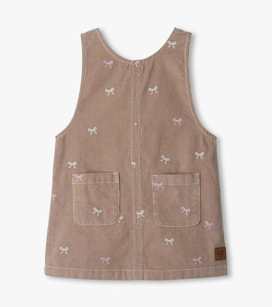 Front view of pink cord pinafore dress with embroidered bows and two front patch pockets