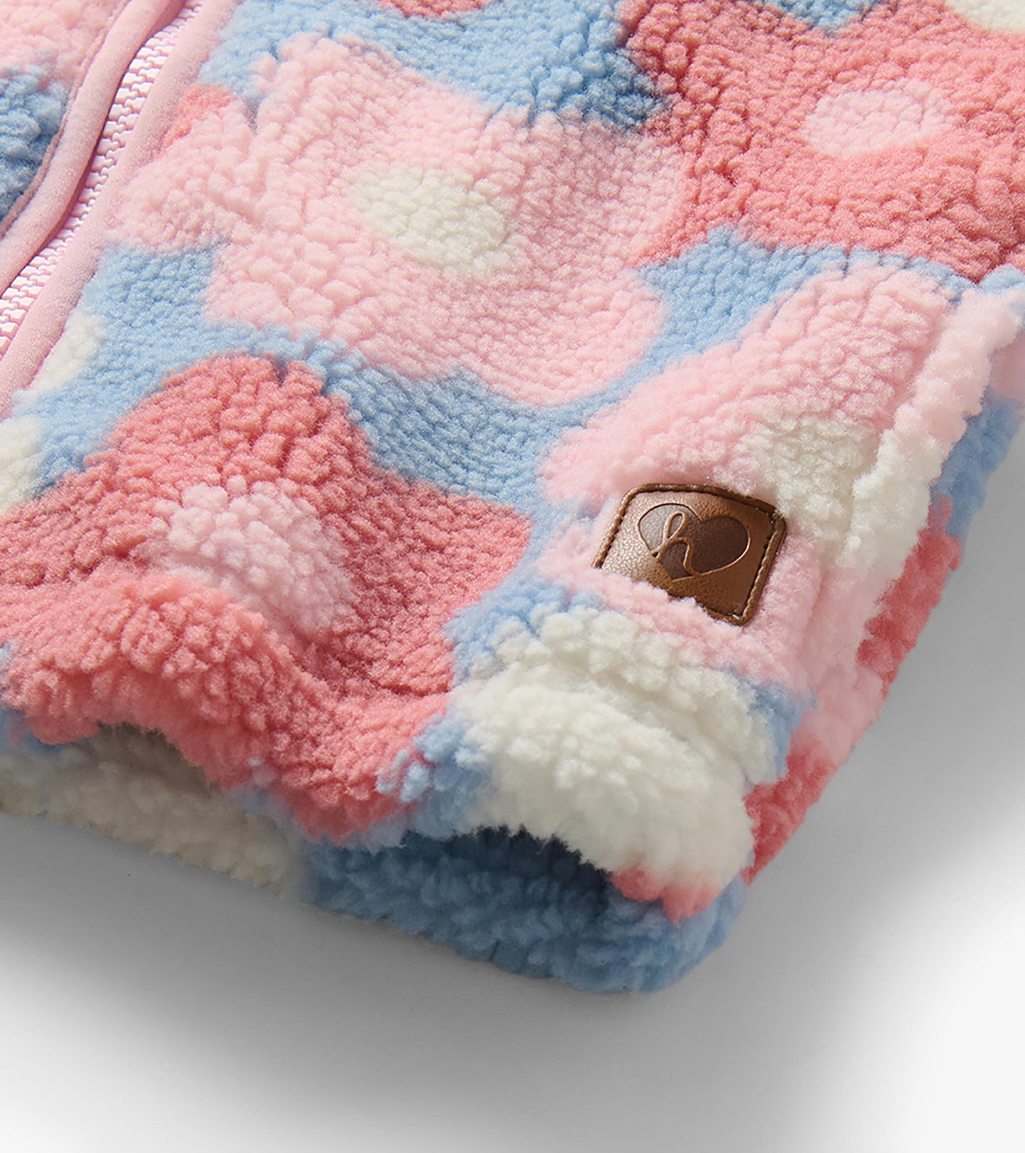 Close-up of sherpa jacket showing pink zipper, large flower print and small logo patch near the hem