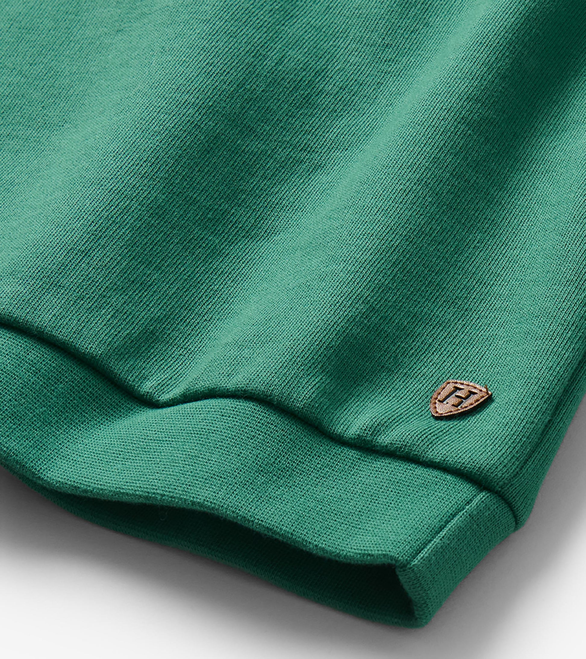 Close-up of green sweatshirt hem with ribbed band and small shield patch