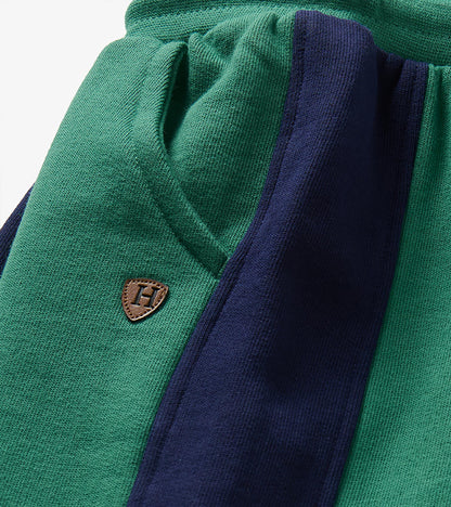 Close-up of bottle green track pants showing front pocket, navy side panel and small H patch