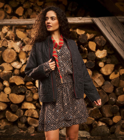Broken ikat smocked waist dress layered under a dark quilted jacket, front view with tiered skirt