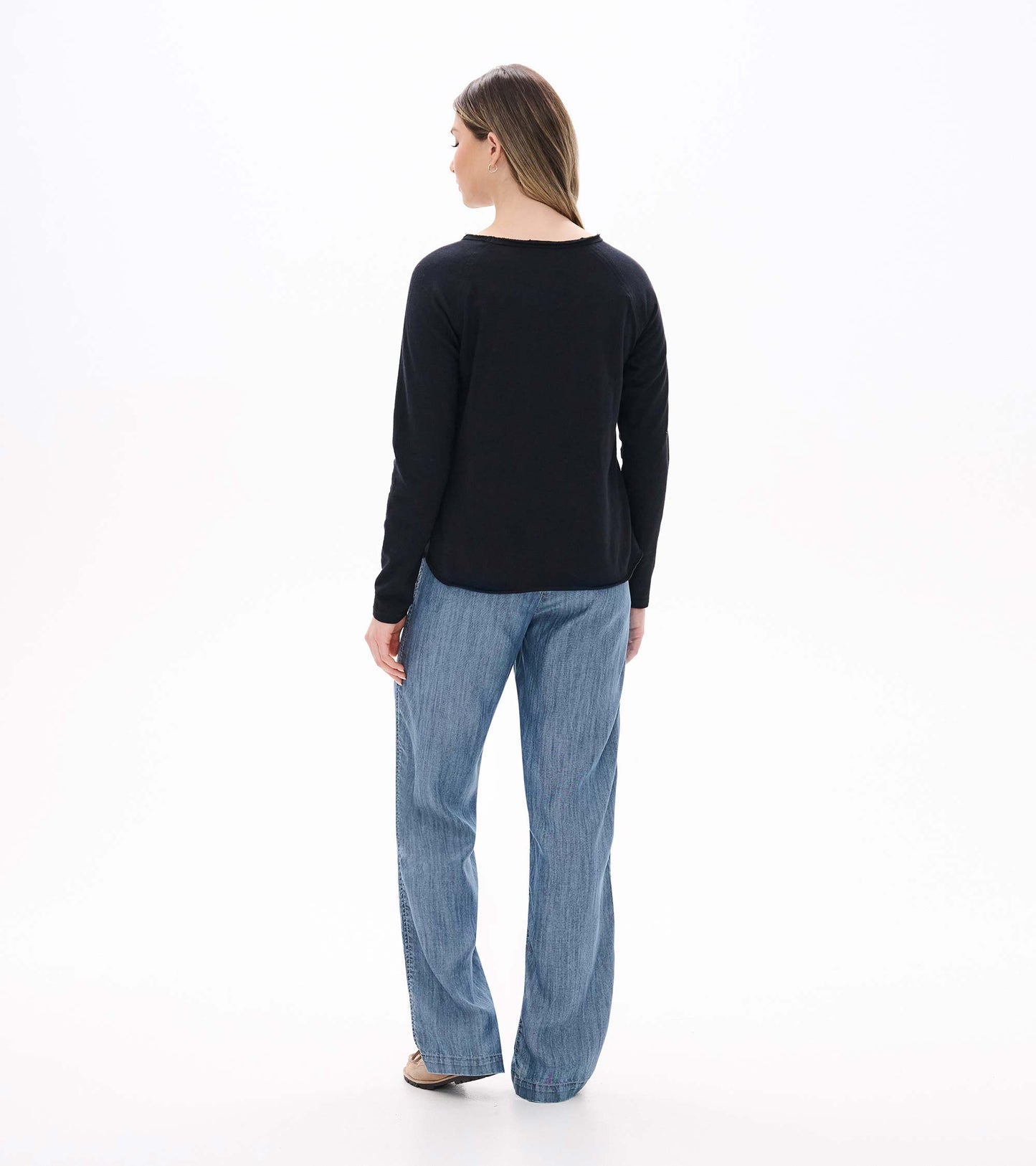 Back view of black raglan sleeve tee on model with long sleeves and curved hem