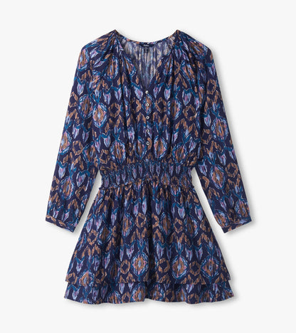 Close-up of blue textured ikat dress with buttoned V-neck, long sleeves, smocked waist, and tiered skirt