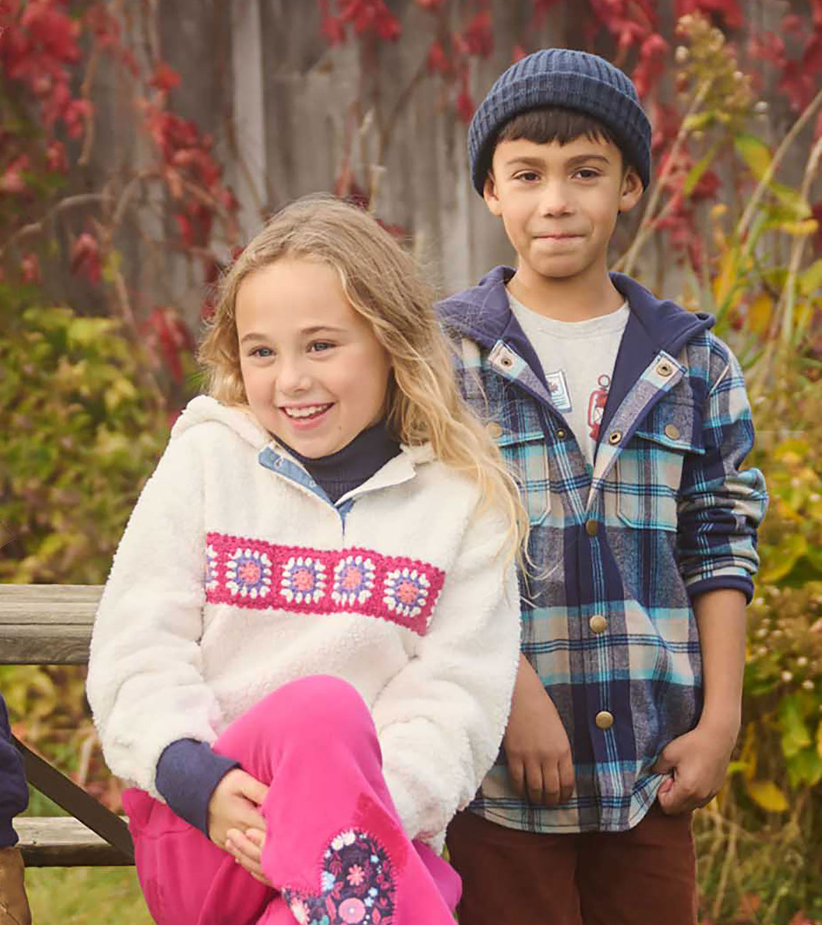 Girl wearing a cream hooded pullover with colorful crochet chest band, seated outdoors