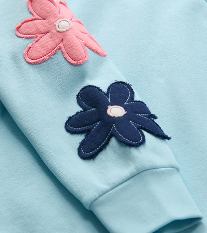 Close-up of sleeve flower appliqués in pink and navy on the cool blue pullover