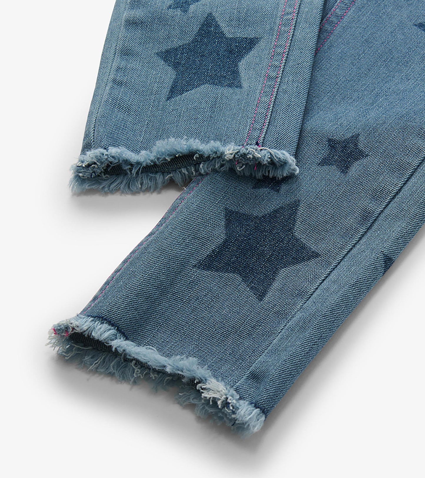 Close-up of blue jeans legs with dark star print, pink side stitching, and frayed hems