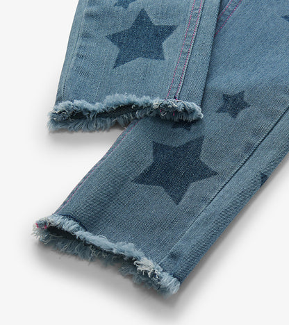 Close-up of blue jeans legs with dark star print, pink side stitching, and frayed hems