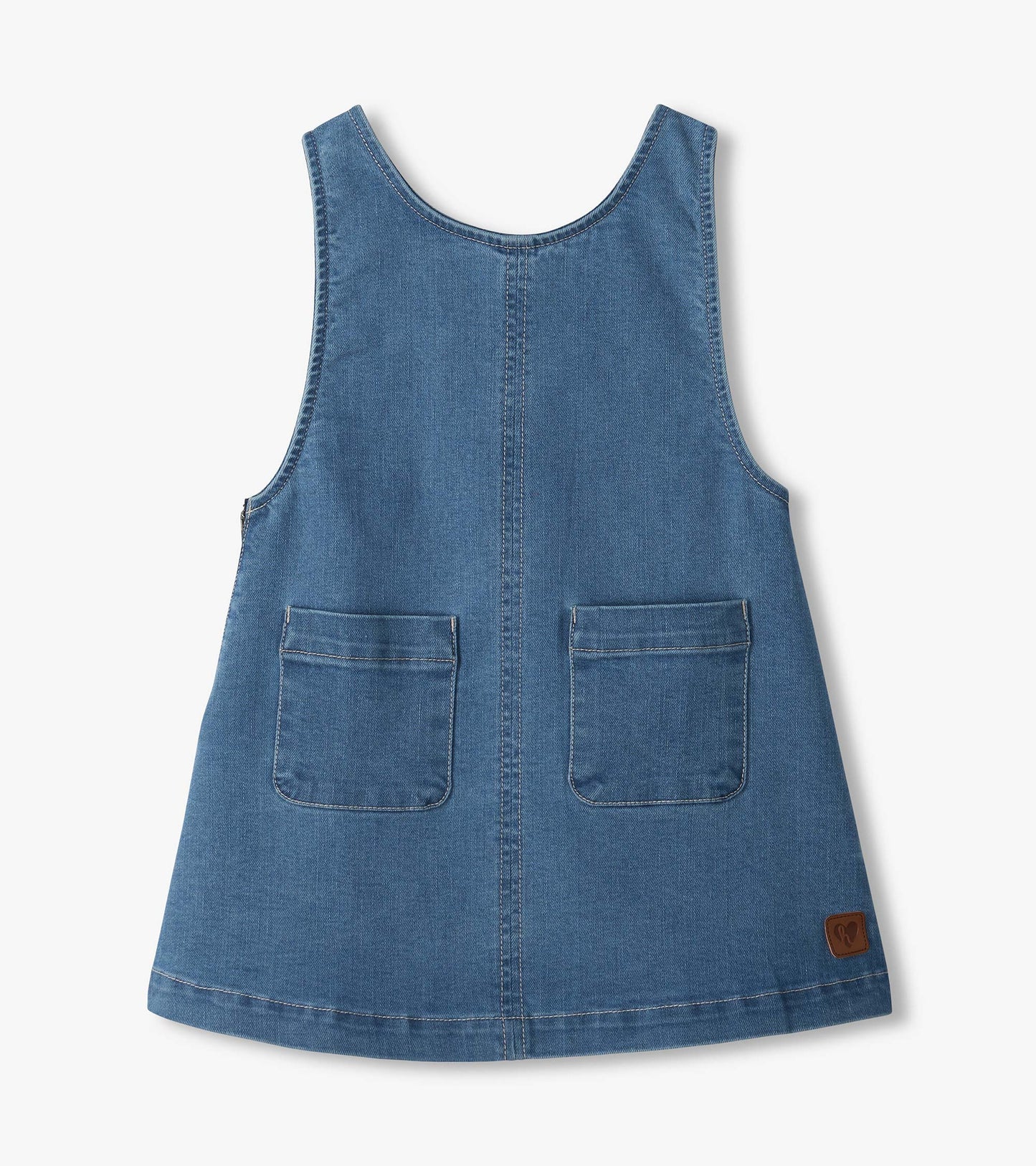 Front view of girls medium-wash denim pinafore dress with wide straps, center seam, and two patch pockets