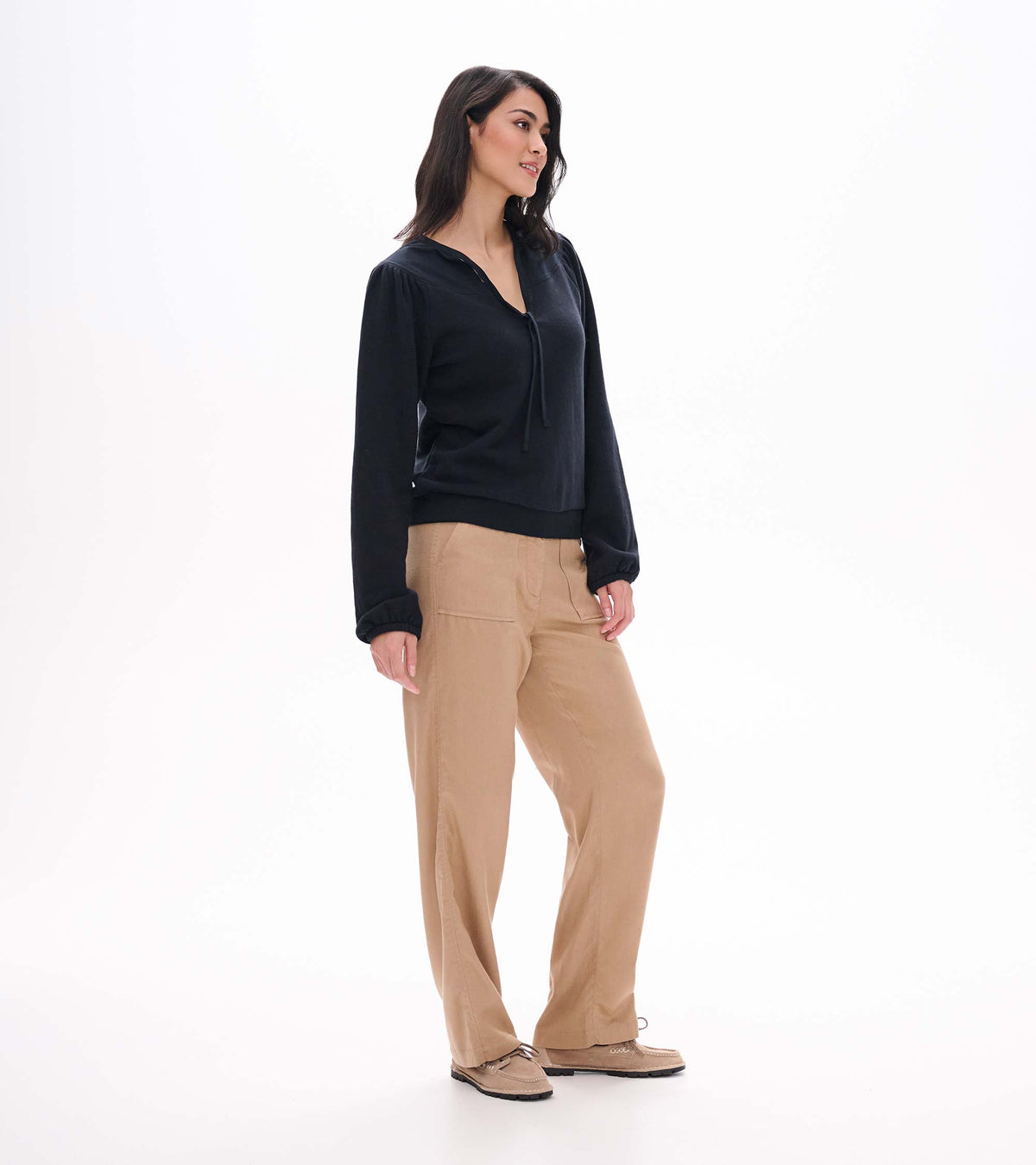 Black long sleeve top shown in side view with tie neckline, gathered shoulders and banded hem