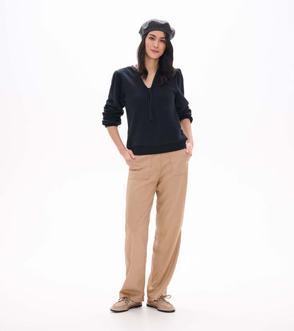 Black long sleeve top with tie neckline and banded hem, shown from the front with sleeves pushed up