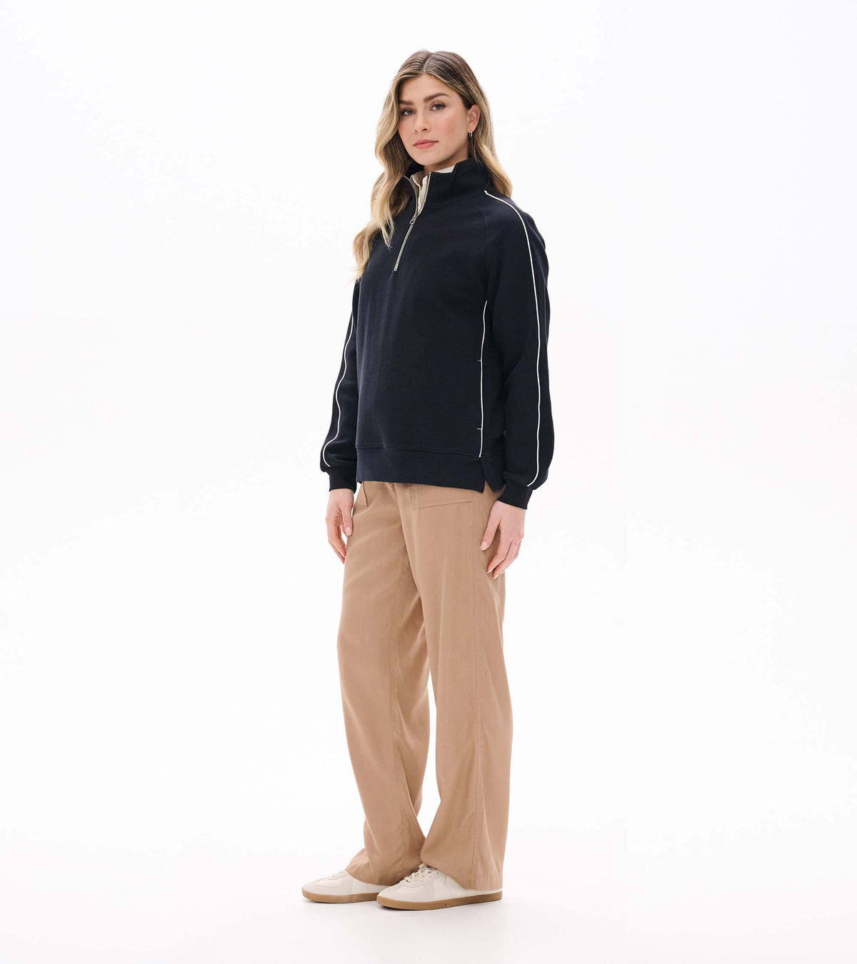 Three-quarter front view of black 1/4 zip knit top with white sleeve piping and side slit hem