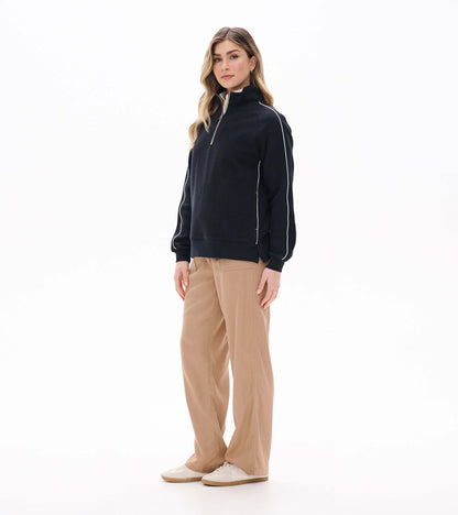 Three-quarter front view of black 1/4 zip knit top with white sleeve piping and side slit hem