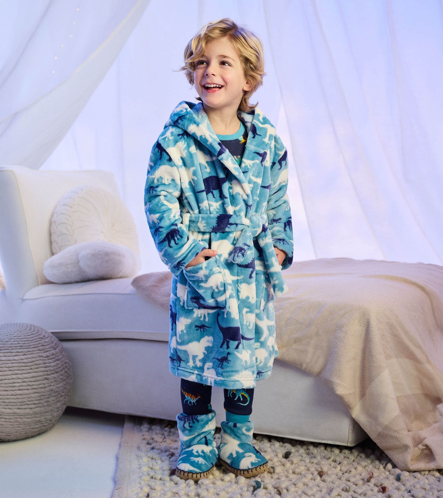 Child wearing blue dinosaur print robe and matching slipper boots in a bedroom setting