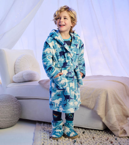 Child wearing blue dinosaur print robe and matching slipper boots in a bedroom setting