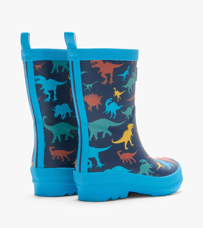 Back angled view of navy rain boots with colorful dinosaur print, blue pull tabs, and blue soles