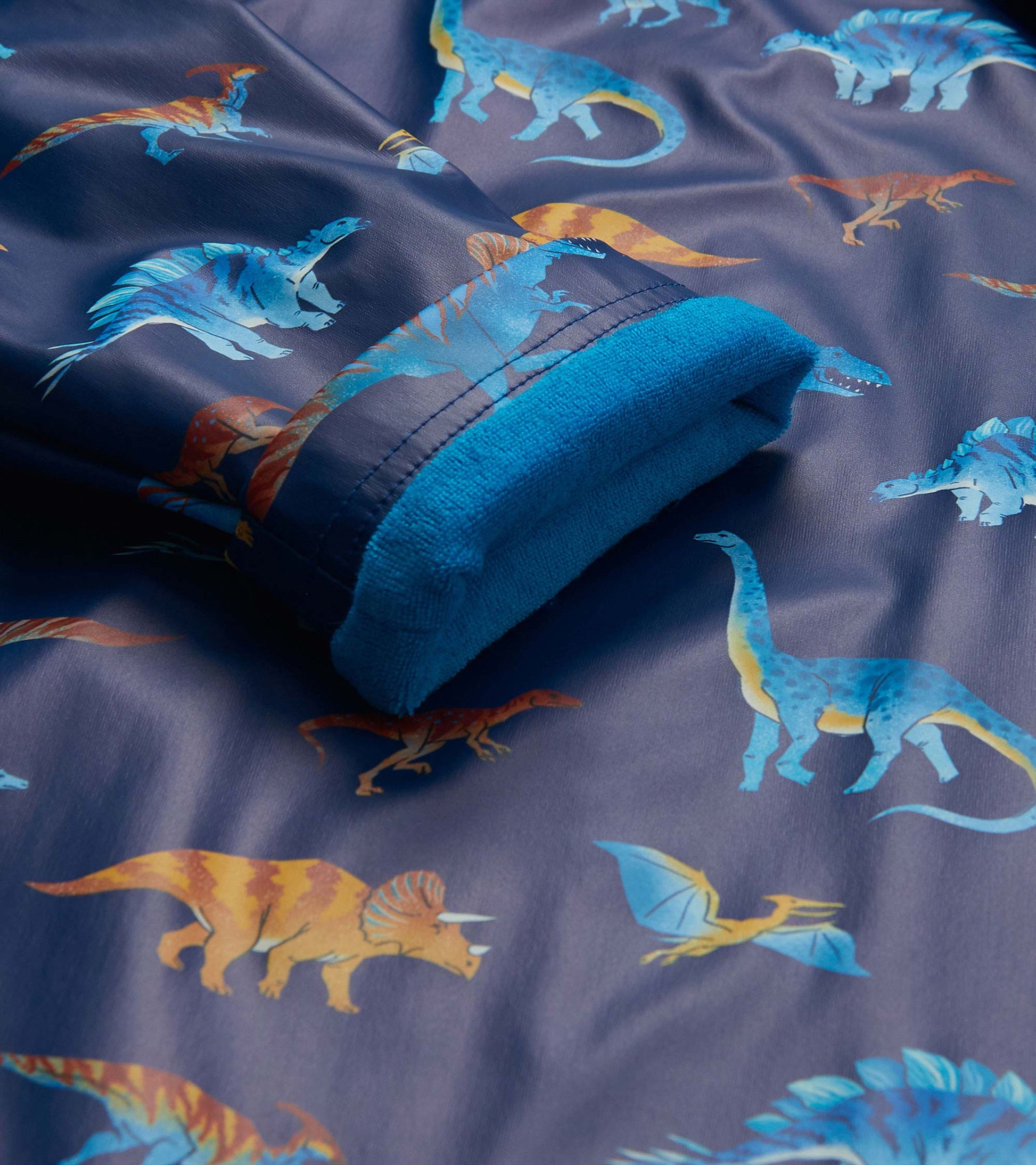 Close-up of the rain coat cuff with blue lining and colorful dinosaur print on a dark blue background