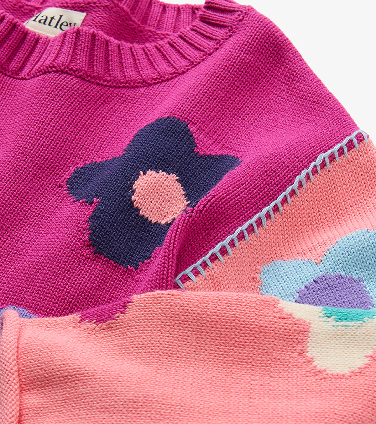 Close-up of pink floral sweater with ribbed crew neck and blue blanket stitching at the shoulder