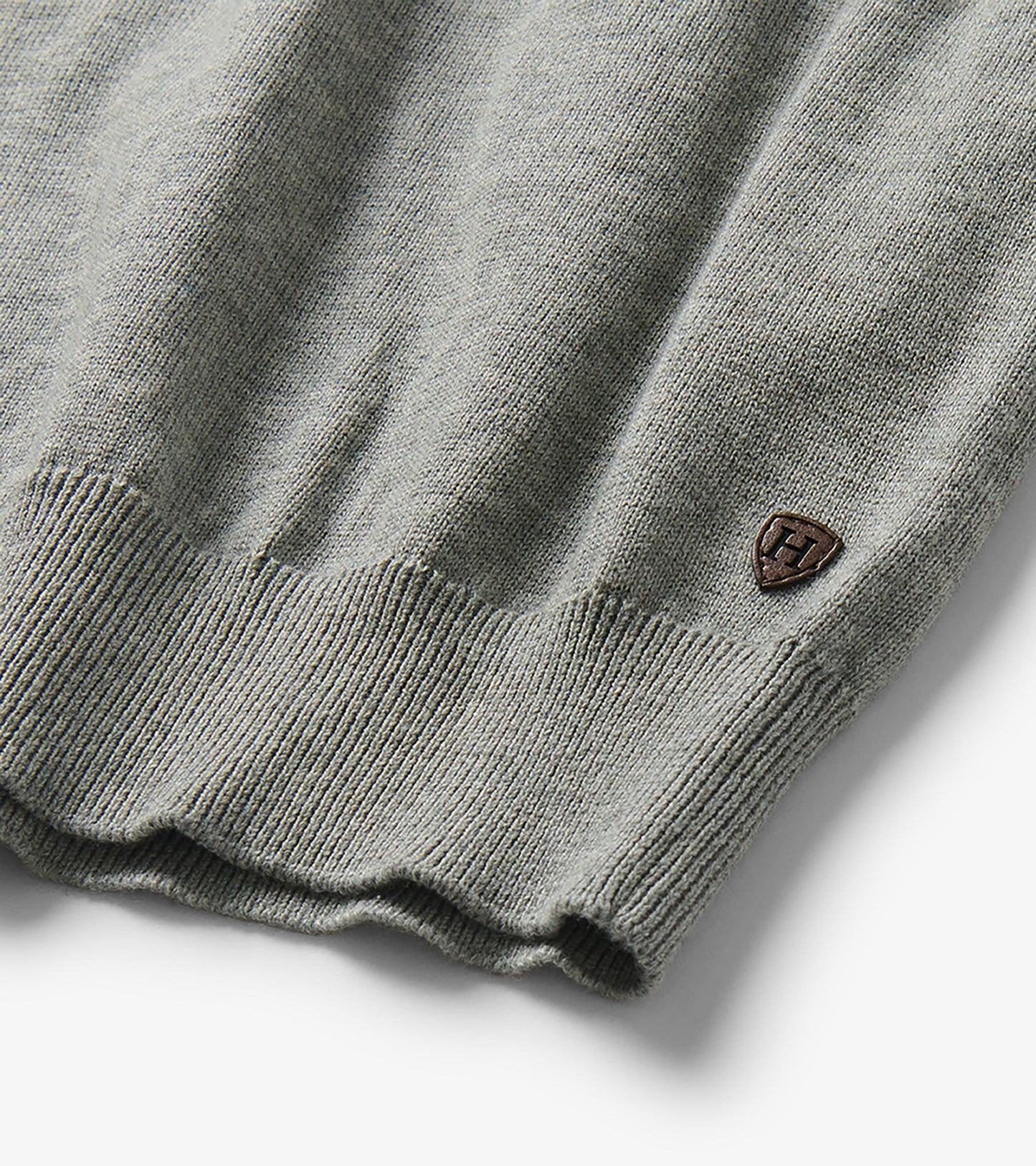 Close-up of the sweater hem with ribbed trim and a small shield-shaped logo patch near the side