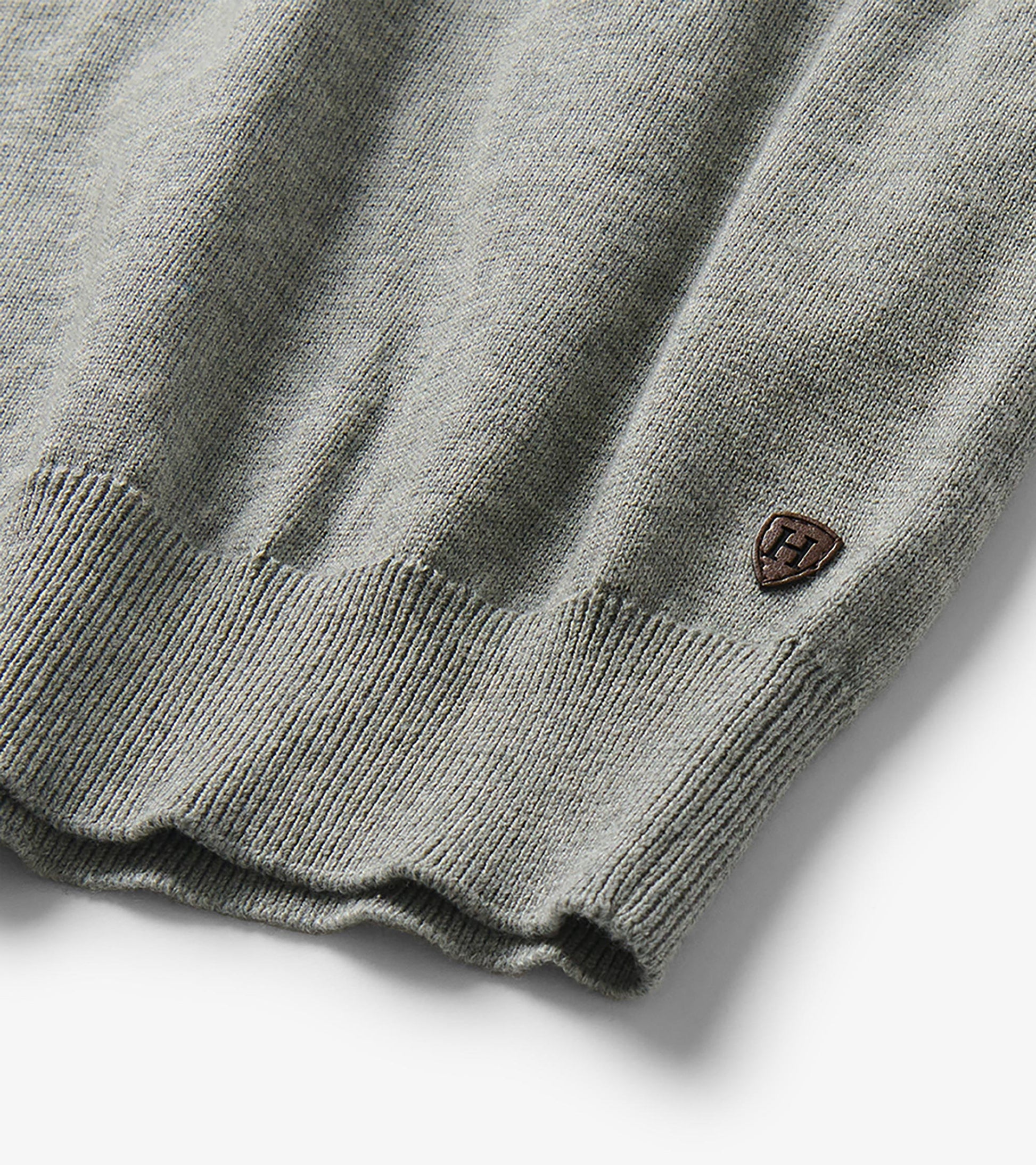 Close-up of the sweater hem with ribbed trim and a small shield-shaped logo patch near the side