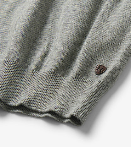 Close-up of the sweater hem with ribbed trim and a small shield-shaped logo patch near the side