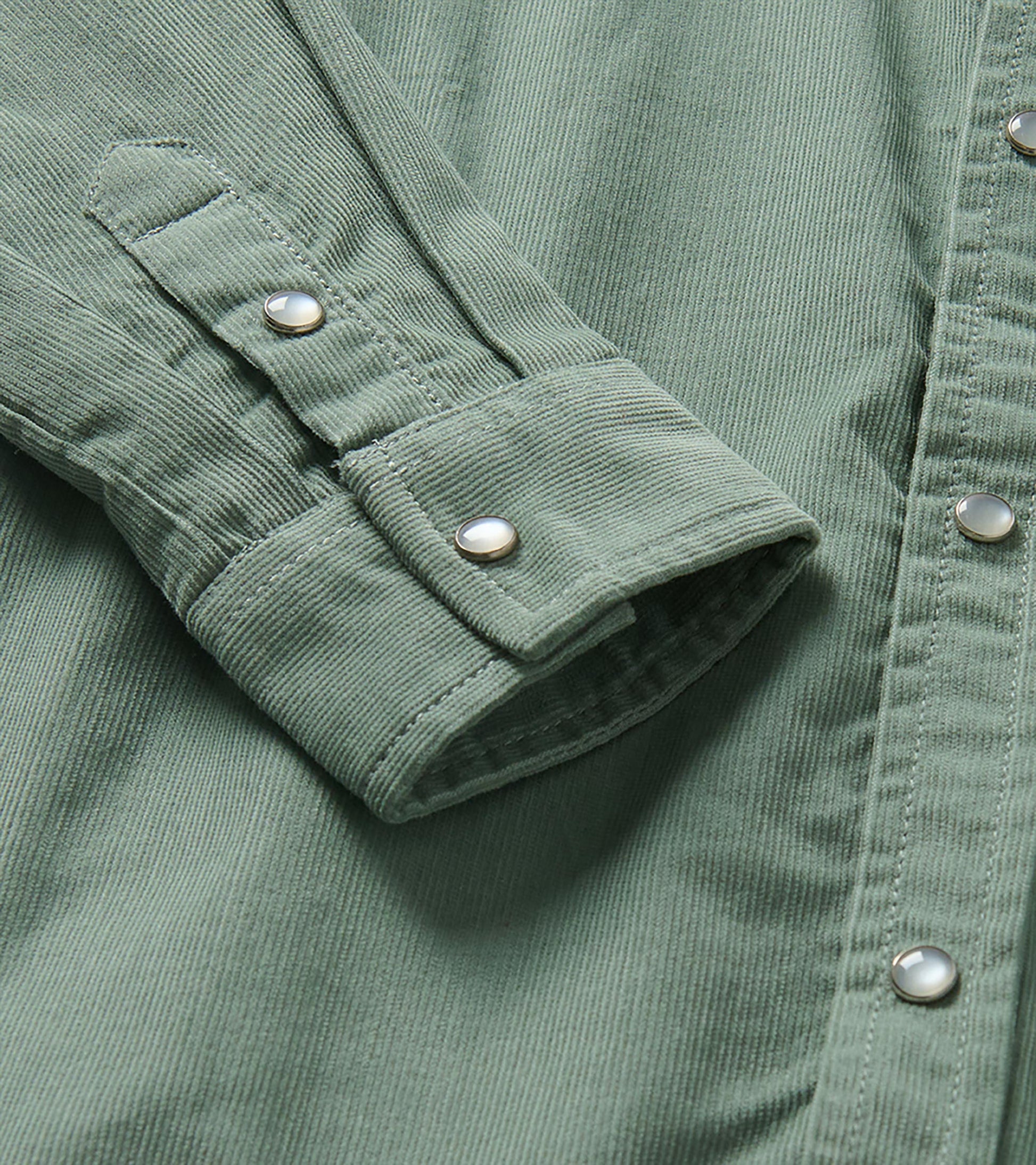 Close-up of green shirt cuff and sleeve tab with pearl snap buttons and fine vertical texture