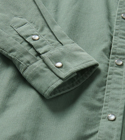 Close-up of green shirt cuff and sleeve tab with pearl snap buttons and fine vertical texture